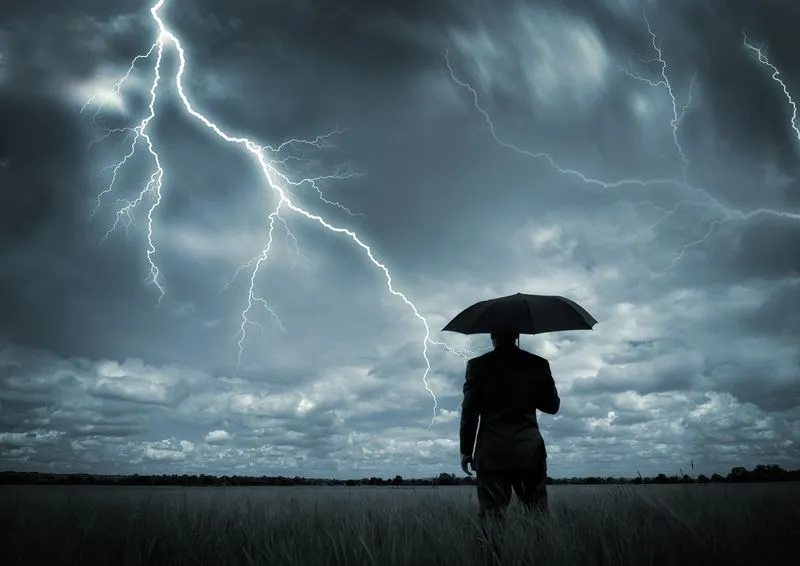 Geschäftsmann mit Regenschirm steht vor einem Unwetter
