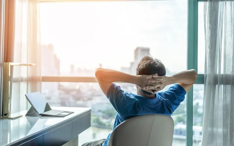 Mann schaut entspannt mit den Händen hinterm Kopf aus dem Fenster
