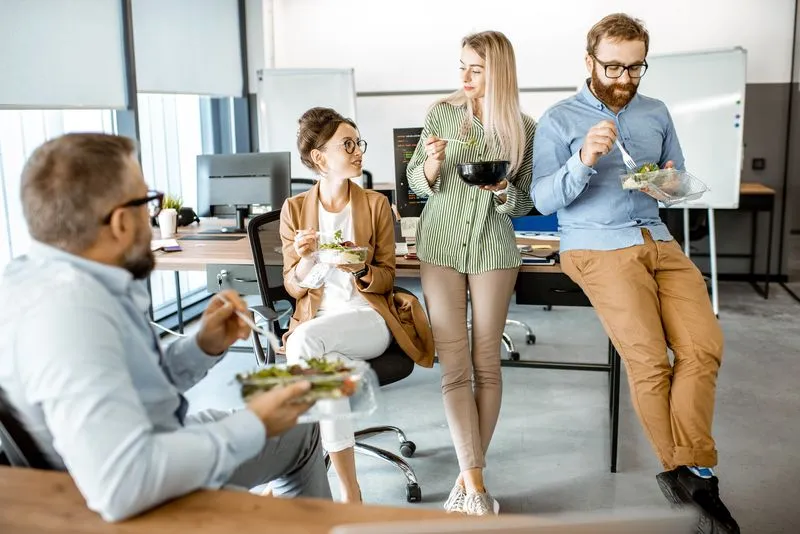 Gruppe entspannter Büroangestellter isst gemeinsam Salat